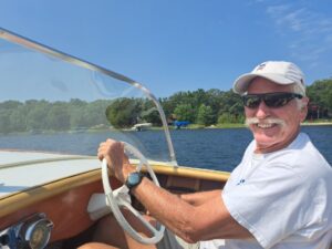 Man smiling while steering a boat on a sunny day.