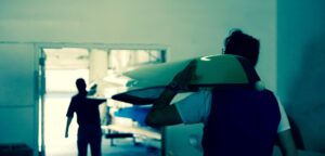Surfer carrying a surfboard in a dimly lit room.