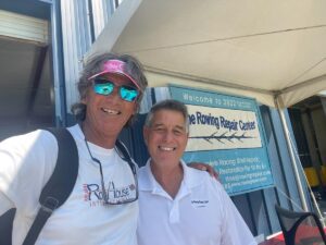 Two smiling people pose in front of a business banner at an outdoor event.