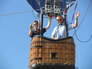 Two men smiling and waving from a hot air balloon basket.