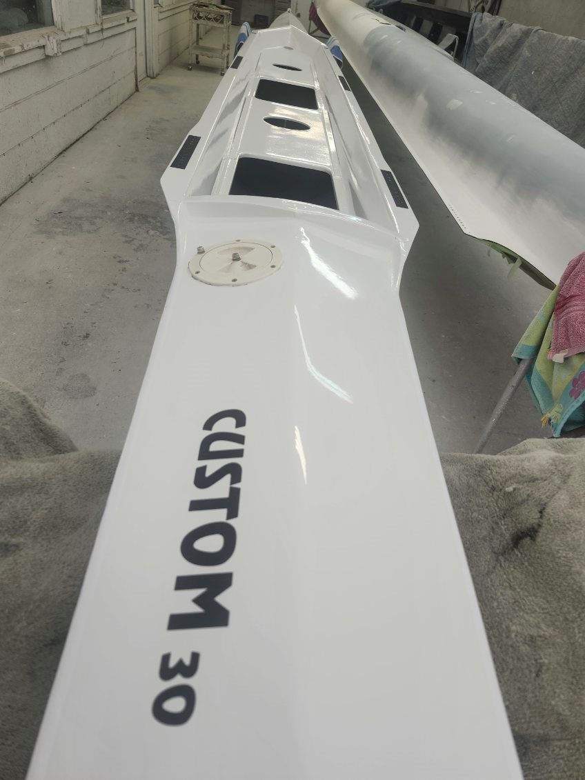 White custom boat hull labeled 'CUSTOM 3' in a workshop.