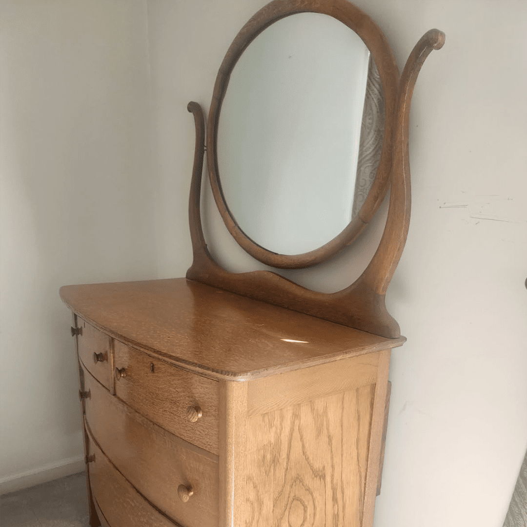 Wooden dresser with an oval mirror and curved edges.