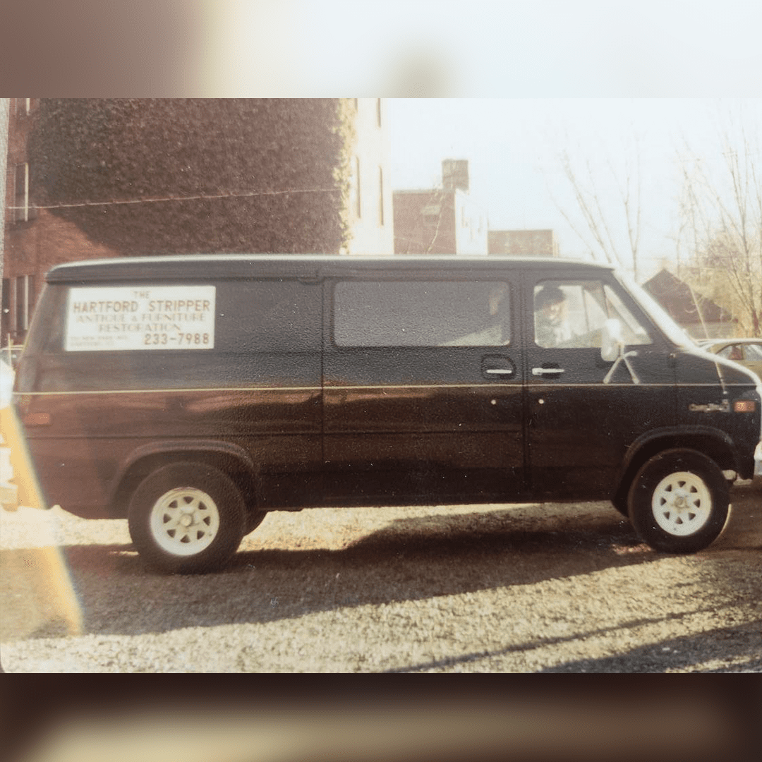 A black van parked outside on a sunny day with a sign on its window.