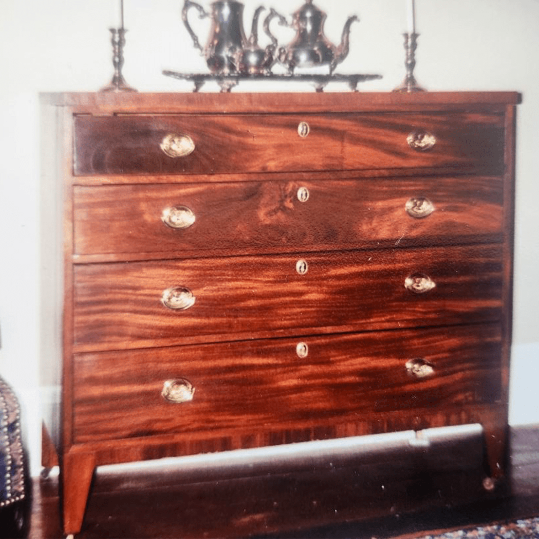 Antique wooden chest of drawers with ornate handles and a decorative item on top.