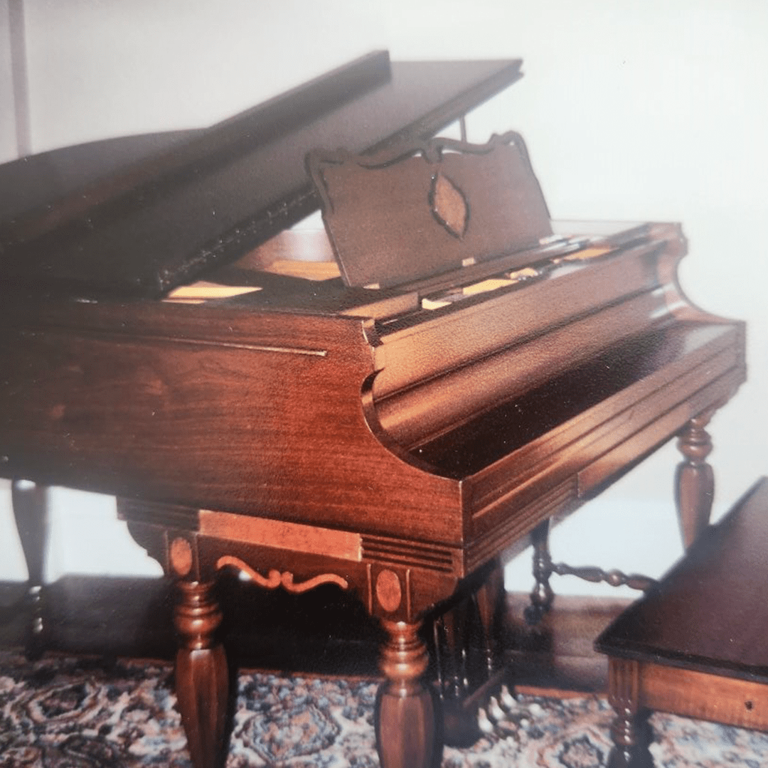 Vintage wooden grand piano with intricate legs and matching bench.