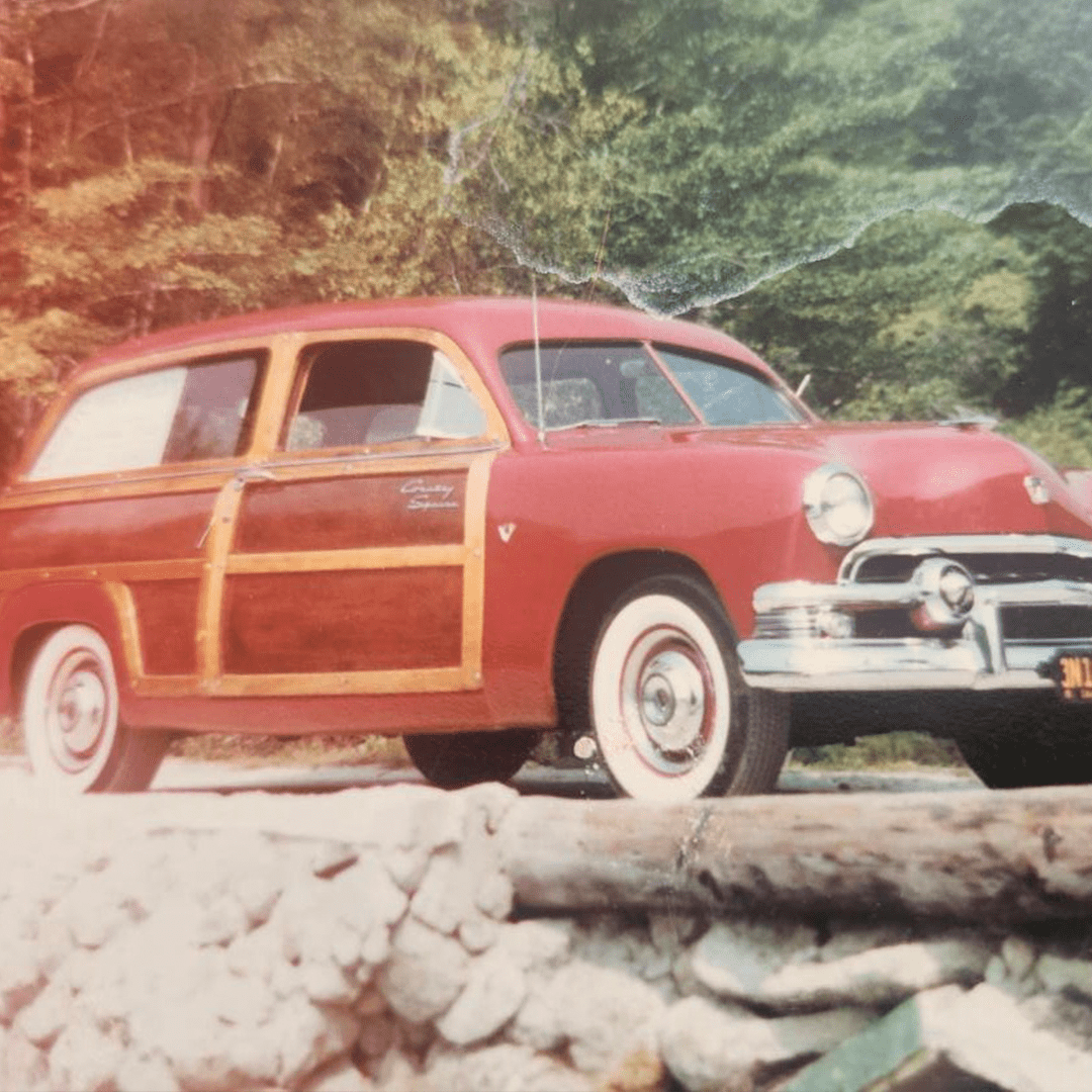 Vintage woody station wagon parked near a forested area.
