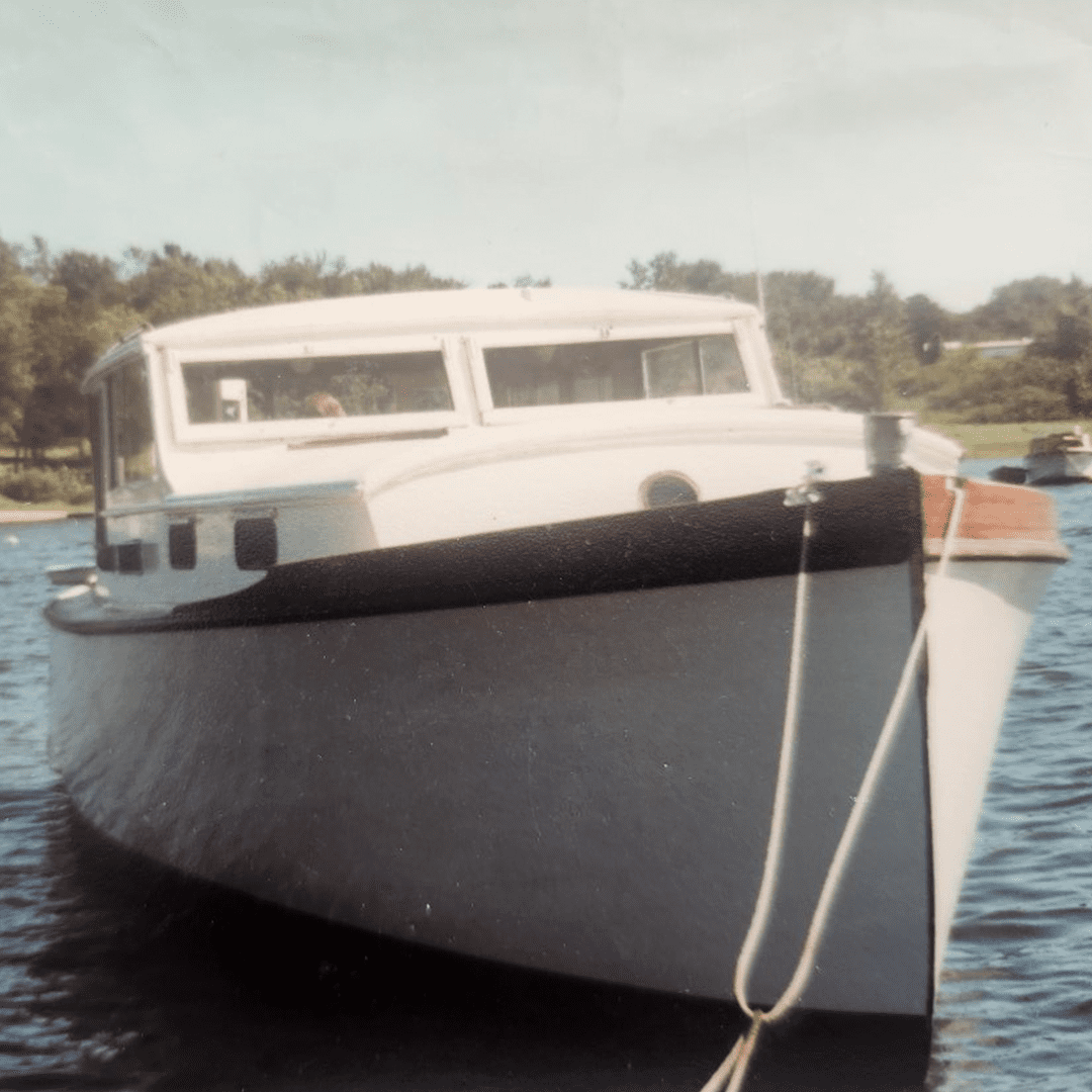 A white boat docked on calm water with trees in the background.