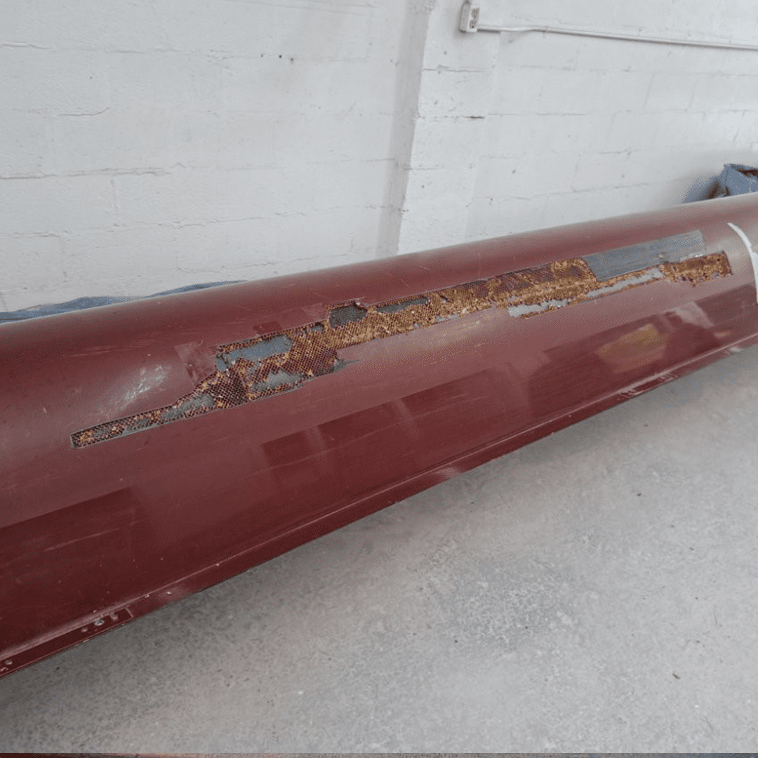 Rusty, scratched red metal pipe or beam on a light floor.