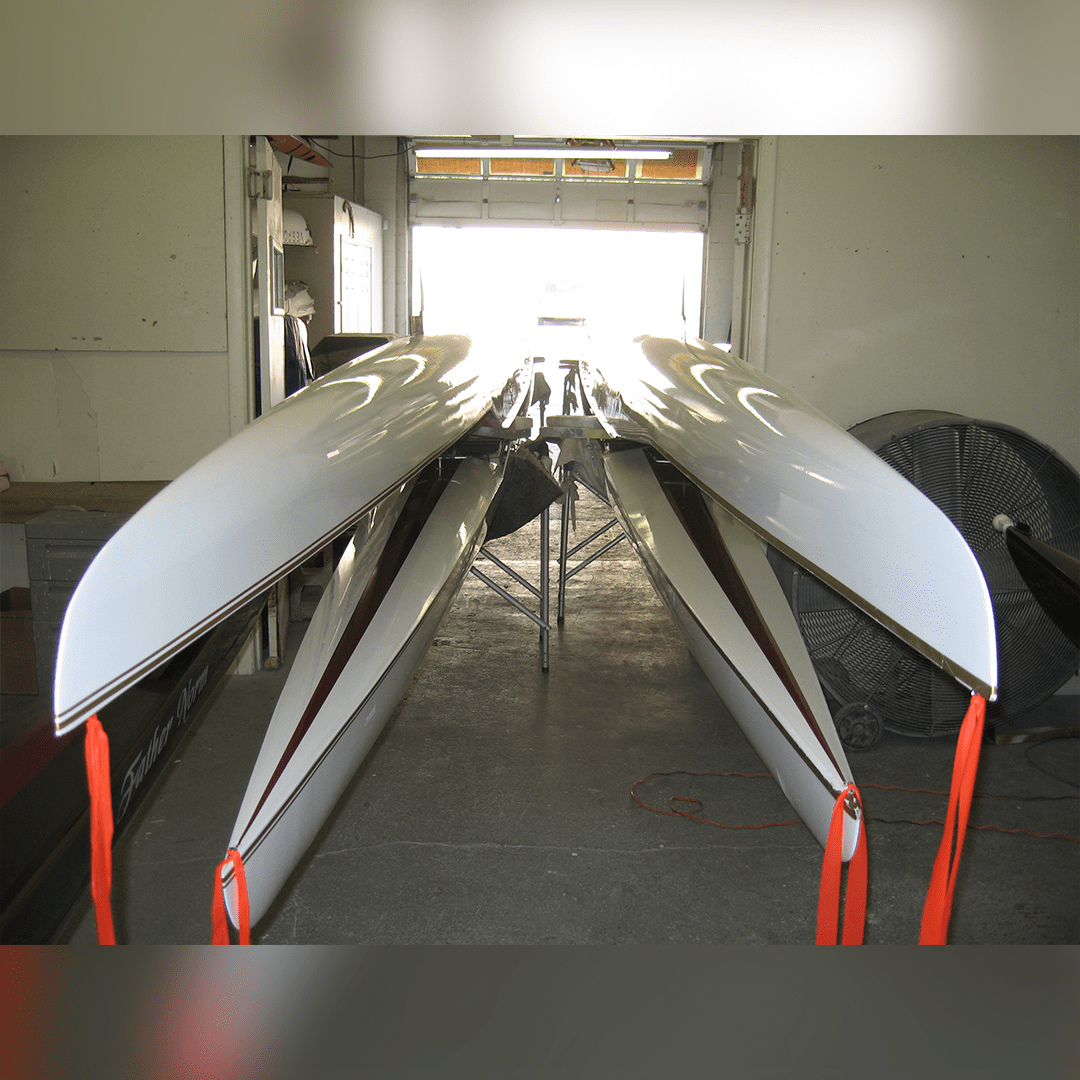 Four rowing shells lined up indoors on racks.