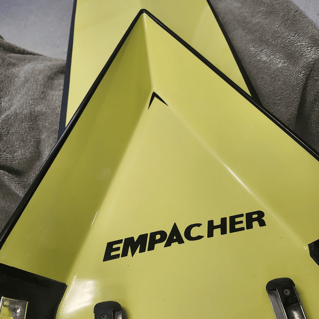 Close-up of a yellow triangular Empacher boat part with black fittings.