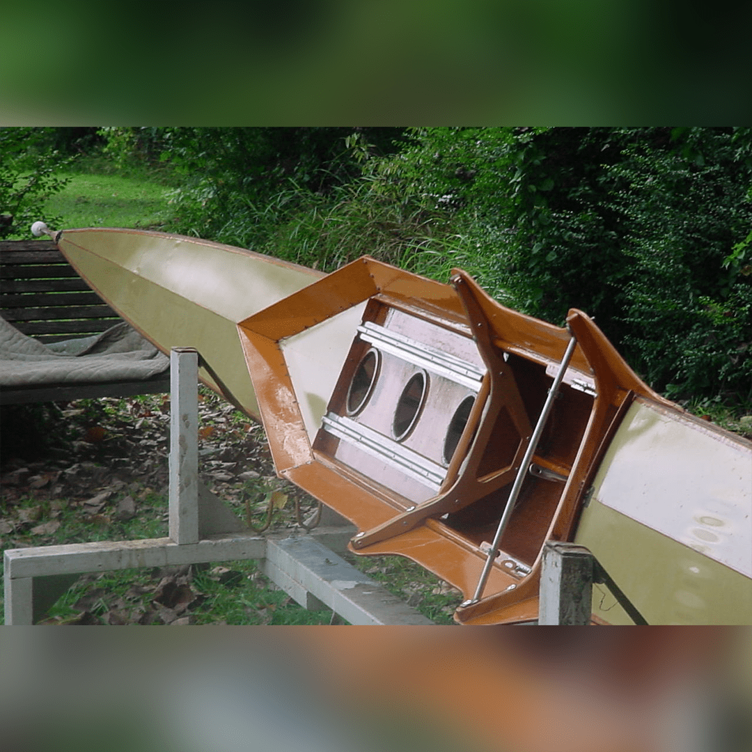Wooden kayak cockpit and seat on a green canoe.