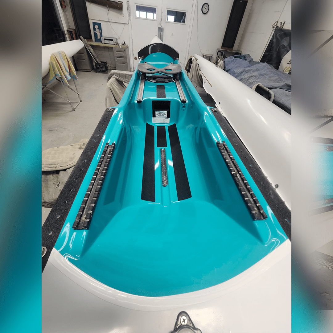 A sleek turquoise kayak with black footrests inside, displayed indoors.