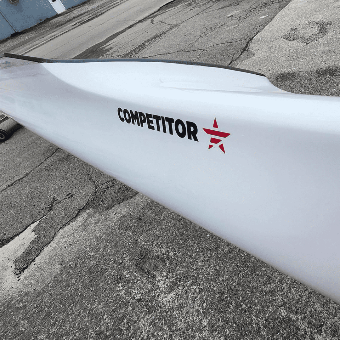 Close-up of a white kayak with 'COMPETITOR' branding on concrete ground.