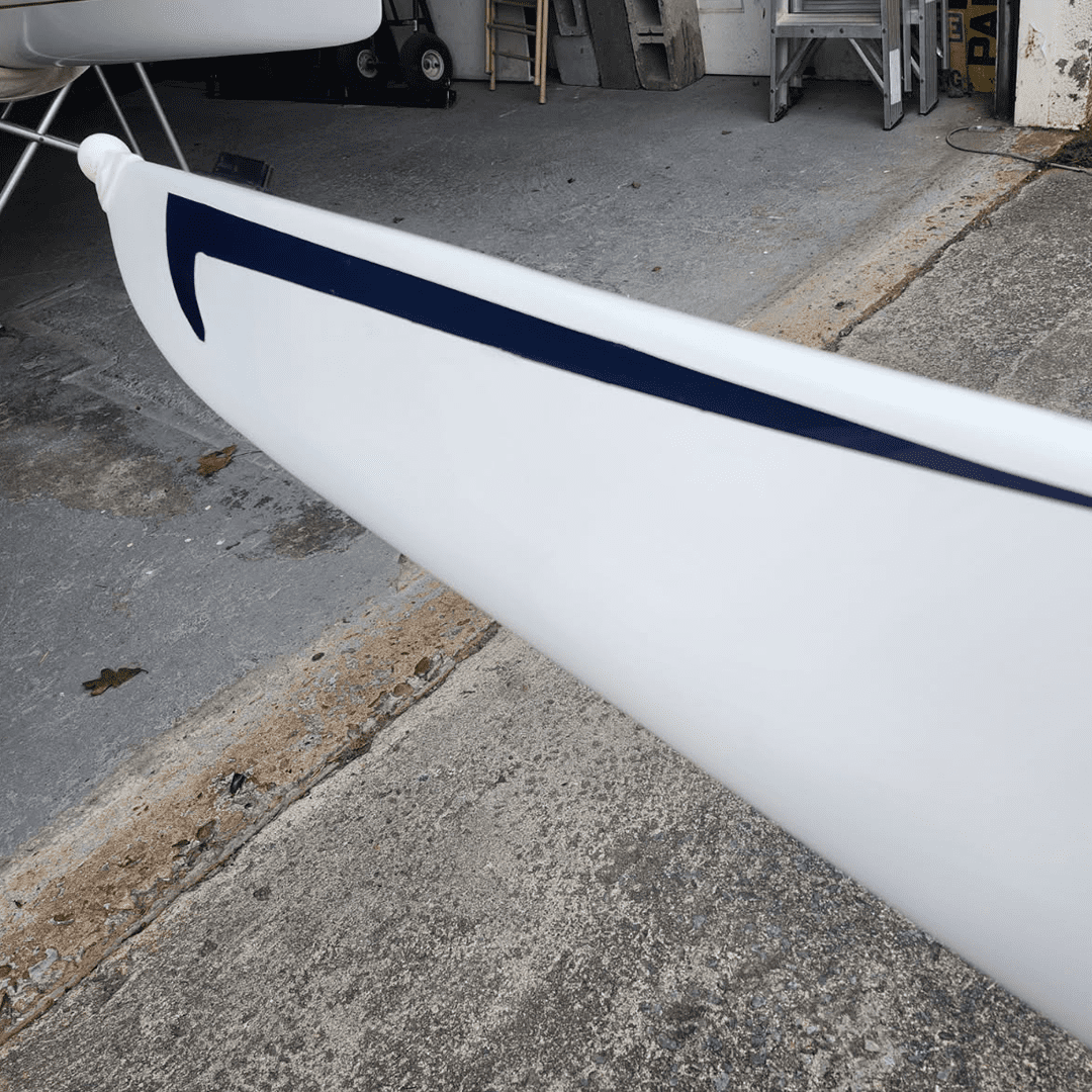 Close-up of a white kayak or canoe with blue markings on a concrete surface.