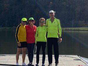 Four people standing together outdoors near water, dressed in sporty casual wear.