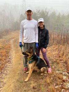 A couple with a German Shepherd on a foggy forest trail.
