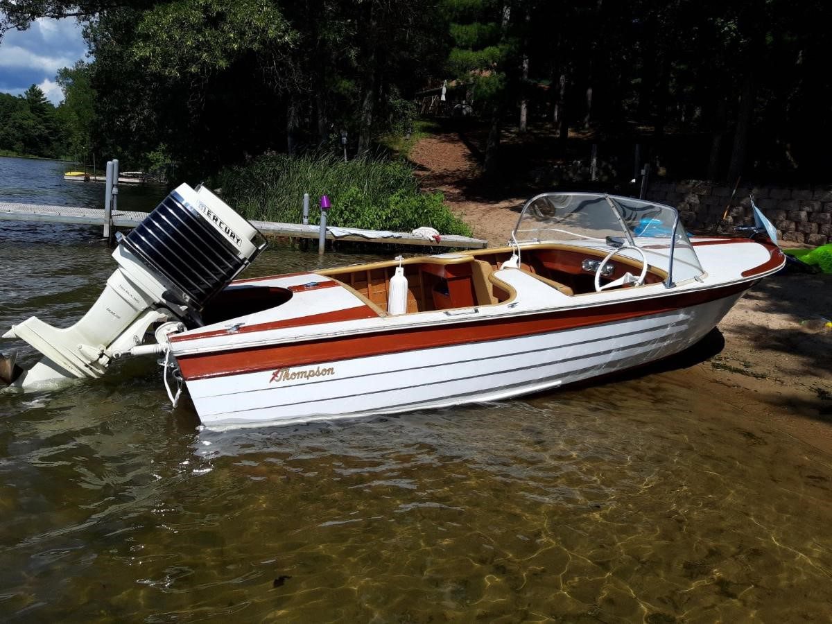 A vintage wooden motorboat with an outboard engine docked in shallow water.
