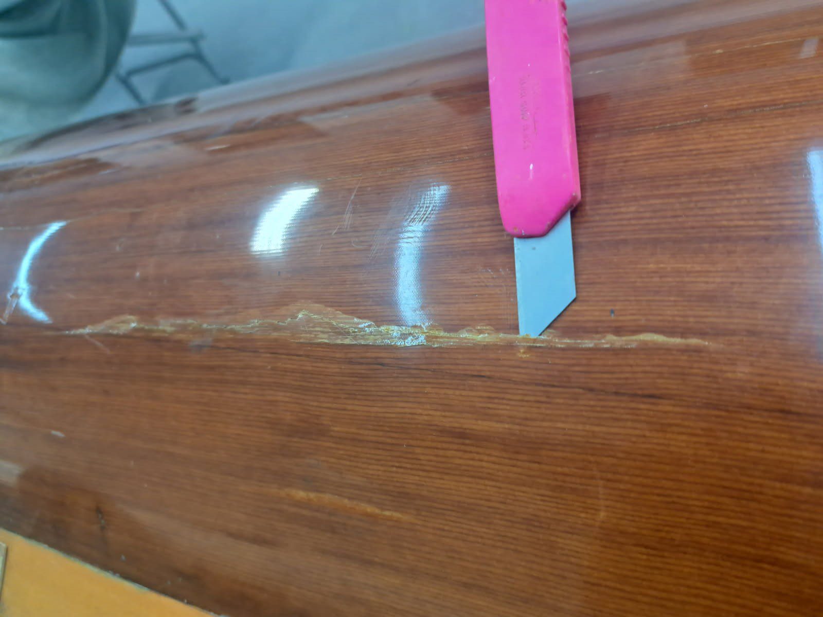 A pink utility knife cutting a wooden surface.